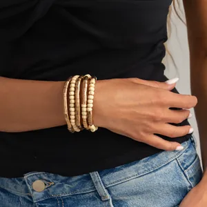 Close-up detail of stacked metallic gold and cream beaded bracelets on a woman's wrist