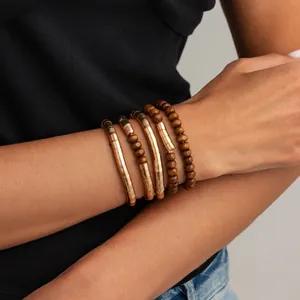 Close-up of stylish stacked gold-toned textured metal and wooden bead bracelets on a wrist