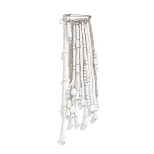 Close-up detail of a stylish fashion brooch featuring white beaded tassels and silver chains