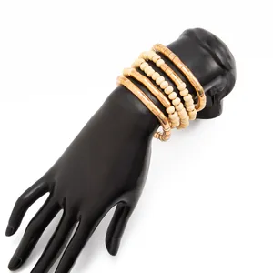 Close-up of layered gold metallic bangles and cream bead bracelets on a black mannequin