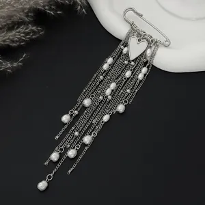 Close-up of a silver safety pin brooch with hanging chains, heart charm and faux pearls
