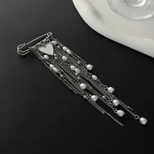 Close-up of silver-tone safety pin brooch with heart pendant and pearl chain tassels.