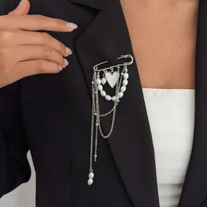Detail view of a silver heart brooch with pearls and chains on a black blazer