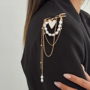 Macro detail of gold-tone brooch featuring imitation pearls, heart pendant and chains