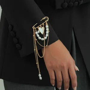 Detail view of heart pendant brooch with imitation pearls and gold chains on a sleeve