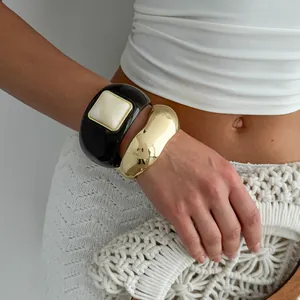 Detail view of chunky black resin and polished wavy gold bangles on a model's wrist