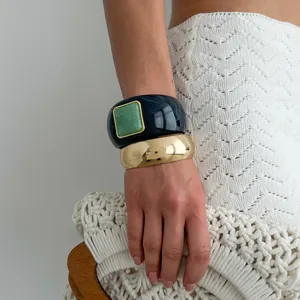 Detail showing chunky black resin bangle with green stone and retro gold cuff bracelet.