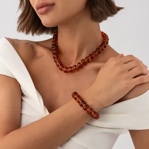 Close-up detail of amber-style resin bead necklace and bracelet set on female model.