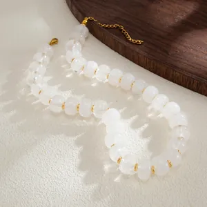 Close-up detail of white translucent resin beads and gold spacers on a textured surface