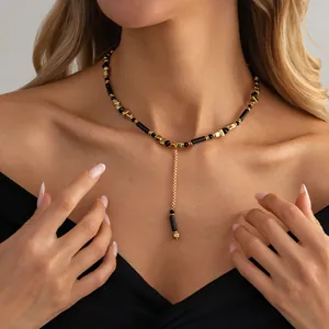 Detail van Y-vormige ketting met gouden kubuskralen en zwarte cilinders op een model.