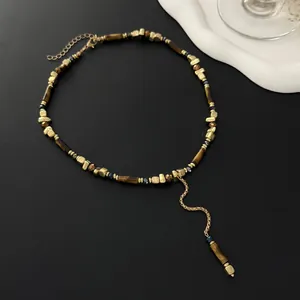 Elegante Y-vormige kralenketting met gouden kubussen en tijgeroogkralen op zwart.