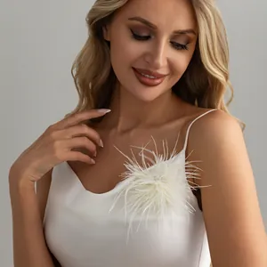 Close-up detail of an elegant white feather brooch pinned to a luxury white silk dress