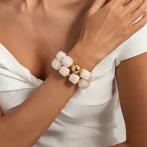 Dettaglio ravvicinato di un bracciale in resina marmorizzata crema con sfera dorata.