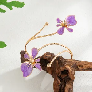Vue détaillée d'un bracelet de bras doré orné de deux fleurs en émail violet exquises.