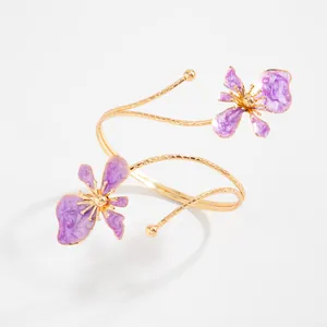 Détail d'un bracelet de bras doré avec fleurs en émail violet et lignes.
