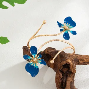 Vue détaillée d'un élégant bracelet de bras doré orné de deux fleurs en émail bleu.