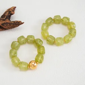 Dettaglio di braccialetti elastici in resina verde chiaro marmorizzata con sfera oro