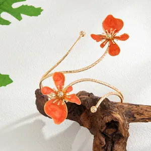Détail d'un bracelet de bras doré avec des fleurs en émail orange vif à texture marbrée.