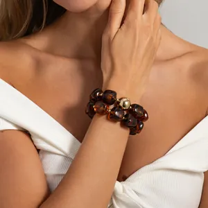 Dettaglio di un bracciale a due fili in resina ambrata con un'elegante perla dorata.