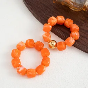 Vista macro di perle in resina marmorizzata arancione e una grande perla dorata sul bracciale