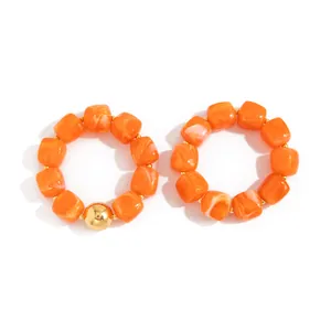 Dettaglio dei braccialetti elastici in resina marmorizzata arancione stile retrò Maillard.
