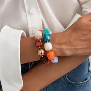 Primo piano di braccialetti colorati in resina marmorizzata indossati con camicia bianca.