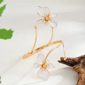 Détail de manchette de bras spirale dorée avec d'élégantes fleurs en émail blanc