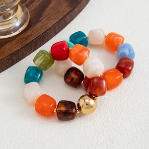 Dettaglio di perle cubiche in resina colorata e una sfera dorata su bracciali elastici