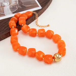 Primo piano di una collana con perle di resina arancione e una grande sfera di metallo dorato