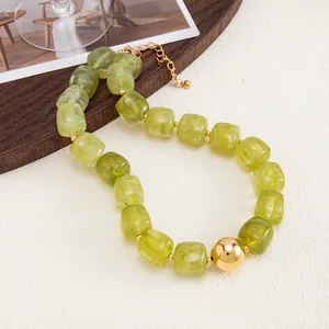 Dettaglio di perle in resina verde oliva traslucide e una grande sfera di metallo dorato