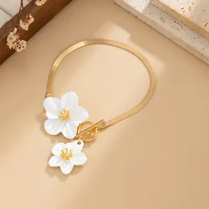 Detailed view of a gold snake chain anklet with white floral charms and OT buckle.