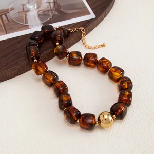 Dettaglio di collana in resina ambrata con grandi perle e una sfera dorata centrale