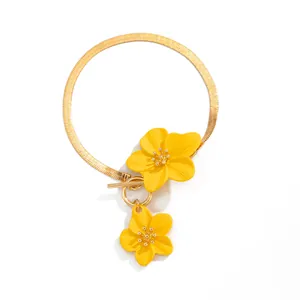 Macro detail of gold snake chain anklet with vibrant yellow flower charms and OT clasp