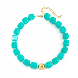 Dettaglio di collana bohémien con perle in resina turchese e un grande accento dorato.