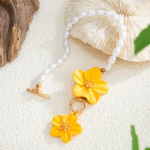 Close-up detail of vibrant yellow enamel flowers and white pearls on a beach-style anklet.