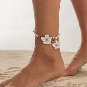 Elegant pearl anklet with white flower charms and OT buckle on a beach background.