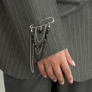 Detailed view of silver safety pin brooch with black beads and heart tassel on grey blazer