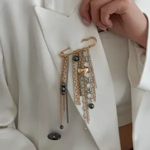 Macro detail of a stylish gold heart tassel safety pin brooch on a white blazer