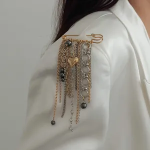 Close-up of stylish metal tassel brooch with heart and bead charms on a white blazer