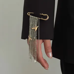 Close-up of a safety pin brooch with silver chain tassels and golden bird charms