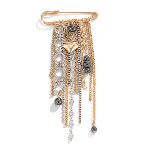 Close-up of golden safety pin brooch with heart charm and metallic tassel chains