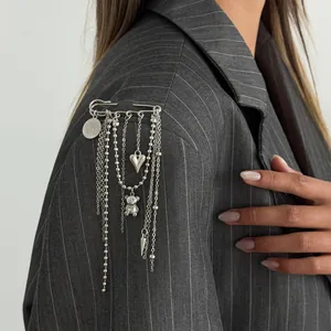 Detailed view of a silver tassel brooch with heart and bear charms on a grey blazer