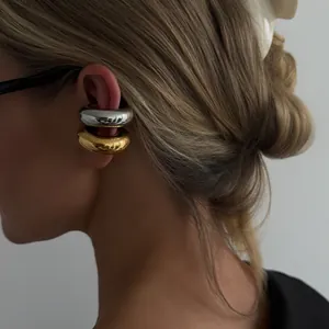 Macro view of model wearing minimalist chunky gold and silver stainless steel ear cuffs.