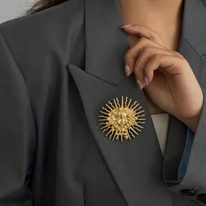 Détail d'une broche relief déesse du soleil dorée épinglée sur un blazer gris élégant