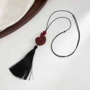 Detailed view of dark red shell pendant with black tassel on thin adjustable cord.