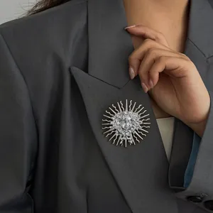 Détail d'une broche en relief déesse du soleil argentée sur un revers de blazer gris.