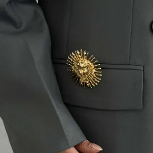 Détail d'une broche dorée avec relief déesse du soleil sur une poche de blazer gris