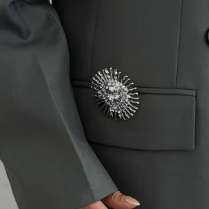 Détail de la broche créative en relief déesse du soleil argentée sur une veste grise.