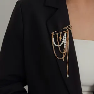 Detailopname van een goudkleurige broche met imitatieparels en een visbedeltje