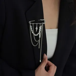 Detail van zilveren veiligheidsspeld broche met parels en vis hanger op een blazer.
